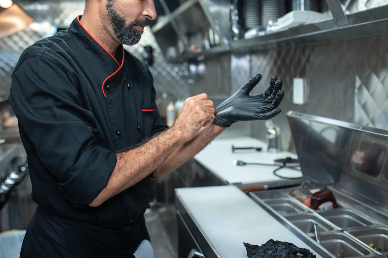 What HACCP Audits Really Check For Chef putting on gloves in a professional kitchen setting, emphasizing hygiene and readiness.